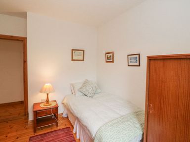 A bedroom with a single bed next to a wooden nightstand with a lamp and three pictures on the wall at Knockbrack Lonart near Killorglin County Kerry