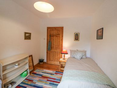 A bedroom with a single bed a wooden door a colorful rug and a small shelf at Knockbrack Lonart near Killorglin County Kerry