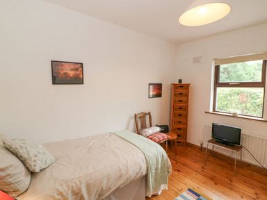 A bedroom with a single bed a chair a tall wooden drawer unit a small TV on a table and a window showing greenery outside at Knockbrack Lonart near Killorglin County Kerry