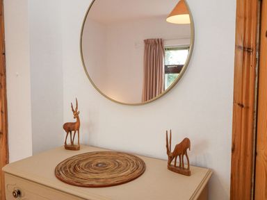 A dresser with two wooden antelope sculptures and a round woven placemat below a round wall mirror at Knockbrack Lonart near Killorglin County Kerry