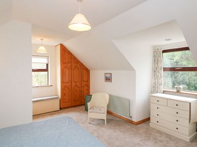 A bedroom with a bed a white chair wooden wardrobe two windows with curtains and a white chest of drawers at Knockbrack Lonart near Killorglin County Kerry
