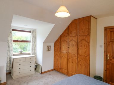 A bedroom with wooden built-in wardrobes a white chest of drawers under a window and a wooden door at Knockbrack in Lonart near Killorglin County Kerry
