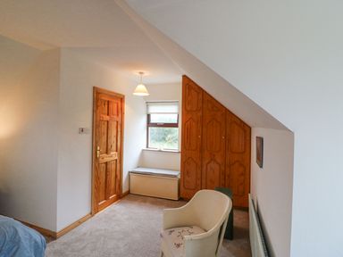 A bedroom with a wooden door a window seat wardrobe and a chair at Knockbrack Lonart near Killorglin County Kerry