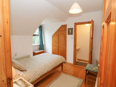 A bedroom with a bed next to a window a wooden wardrobe and a door leading to a small bathroom at Knockbrack in Lonart near Killorglin County Kerry
