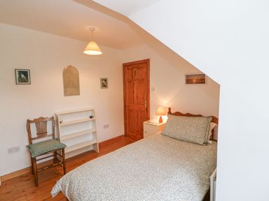 A bedroom with a bed a wooden chair a small white bookshelf a wooden door and a lamp on a nightstand at Knockbrack Lonart near Killorglin County Kerry