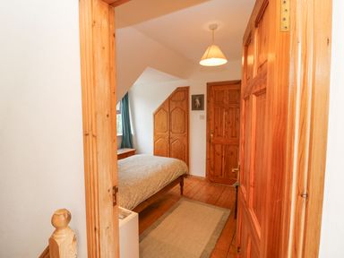 A bedroom with a wooden bed a rug a pendant light wooden doors and a small table under a slanted ceiling at Knockbrack in Lonart near Killorglin County Kerry