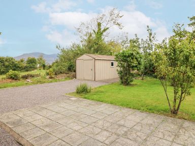 A metal garden shed on a gravel driveway next to a lawn with trees at Knockbrack Lonart near Killorglin County Kerry