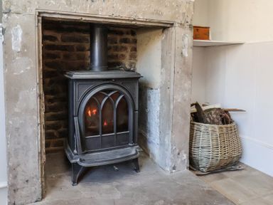 A fireplace with a wood burning stove and a basket of firewood at Field View in Ruswarp