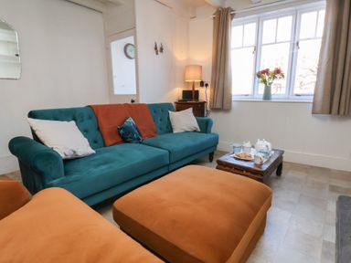 A living room with a teal sofa and orange ottomans near a window with flowers on a wooden coffee table at Field View in Ruswarp
