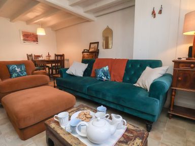 A living room with a green sofa brown armchair and ottoman a wooden coffee table with tea set and cookies at Field View in Ruswarp
