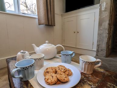A table with a white teapot, four cups, and a plate of cookies at Field View in Ruswarp