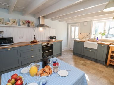 A kitchen with grey cabinets a wooden countertop a white farmhouse sink and a table with a blue tablecloth and breakfast items at Field View in Ruswarp