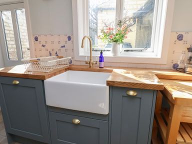 A kitchen sink with a gold faucet and wooden countertops with flowers in a vase on the windowsill at Field View in Ruswarp