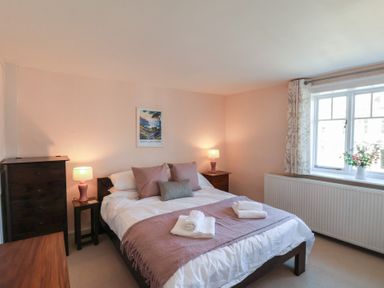 A bedroom with a bed pillows lamps a window with curtains and flowers on the sill at Field View in Ruswarp