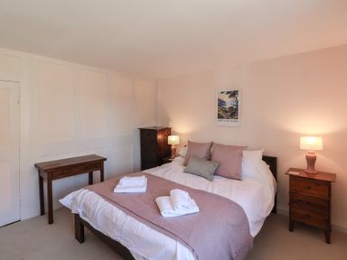 A bedroom with a double bed, bedside tables with lamps, a wooden dresser, and a painting on the wall at Field View in Ruswarp
