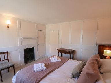 A bedroom with a bed, pillows, folded towels, a wooden chair, a small wooden table, a fireplace, and a wall lamp at Field View in Ruswarp