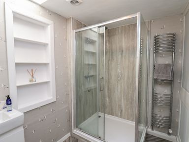 A bathroom with a glass shower enclosure a wall-mounted towel radiator a built-in wall shelf and a small sink at Field View in Ruswarp