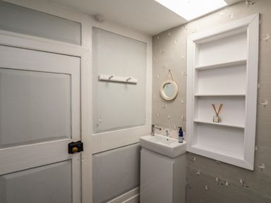 A small bathroom with a white door a wall-mounted sink a round mirror and built-in shelves at Field View in Ruswarp