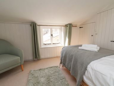 A bedroom with a bed covered by gray bedding a window with green curtains a green armchair and a green rug on the floor at Field View in Ruswarp
