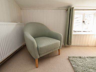 A light green armchair on a carpeted floor next to a radiator and window with green curtains at Field View in Ruswarp