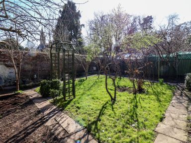 A garden area with grass, small trees, a stone pathway, and a wooden garden arch at Field View in Ruswarp