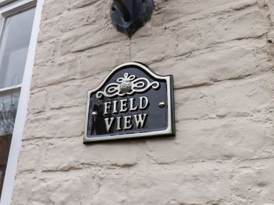 A black and white house nameplate saying Field View mounted on a beige stone wall next to a window at Field View in Ruswarp