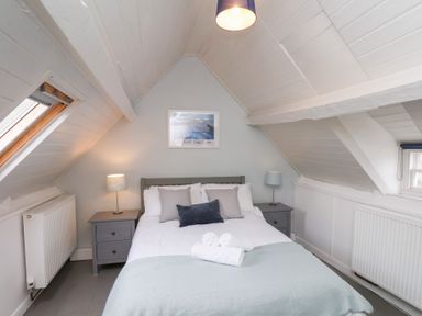 A bedroom with a bed between two bedside tables with lamps under a slanted ceiling at Field View in Ruswarp