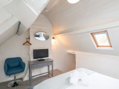 A bedroom with a gray desk, a small TV, a blue chair, a mirror, a skylight window, and a bed with towels at Field View in Ruswarp