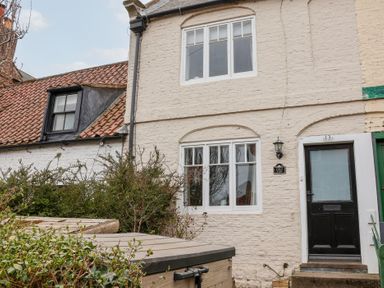 A white brick exterior of a house with windows a black door bushes and a wooden storage box at Field View in Ruswarp
