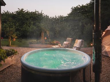 An outdoor hot tub with bubbling water on a gravel patio next to two lounge chairs and greenery at Moonshine in St Erme near Truro