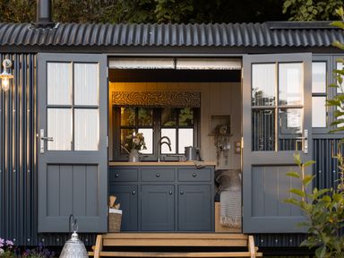 A small kitchen with blue cabinets and a sink inside a structure with open double doors at Moonshine in St Erme near Truro