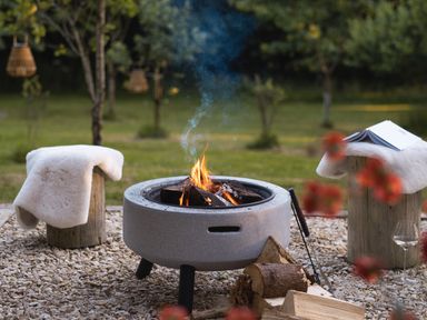 An outdoor fire pit with logs burning and two wooden stools with white covers in a garden at Moonshine in St Erme near Truro