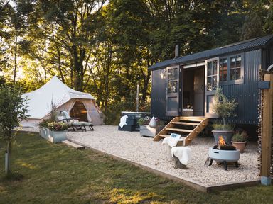 An outdoor area with a tent loungers a small cabin with open doors and a fire pit at Moonshine in St Erme near Truro