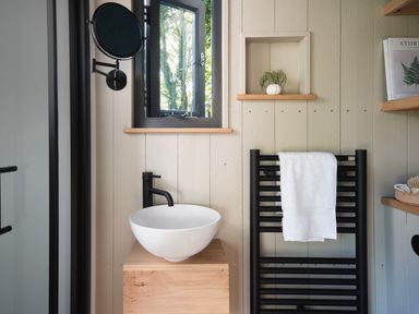 A bathroom with a white sink on a wooden stand a black faucet a black towel radiator with a white towel and a small window at Moonshine in St Erme near Truro