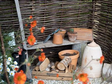 A gardening corner with clay pots trowel logs in a wooden crate and rubber boots behind orange flowers at Moonshine in St Erme near Truro