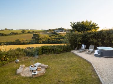 A garden with a fire pit surrounded by stones loungers and a hot tub on a gravel area at Stargazer in St Erme near Truro