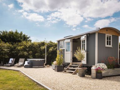 A small cabin with open doors and stairs in a garden with plants and lounge chairs near a hot tub at Stargazer St Erme near Truro