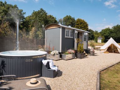 An outdoor area with a hot tub a gray cabin a tent and garden plants at Stargazer in St Erme near Truro