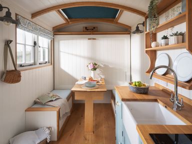 A kitchen area with wooden countertops a sink a table with benches and shelves with plates and plants at Stargazer in St Erme near Truro