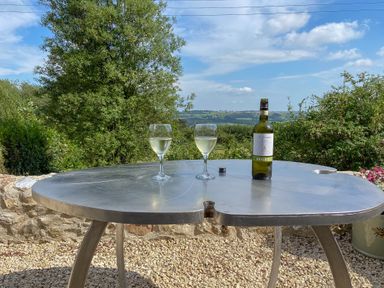 A metal outdoor table with two glasses of white wine and a bottle with a countryside view at The Wheelhouse Beacon near Yarcombe