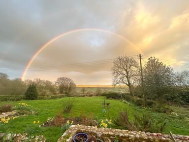 A garden with green grass flowers trees and a rainbow in the sky at The Wheelhouse in Beacon near Yarcombe