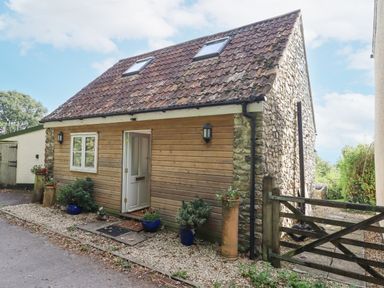 A small house with stone and wood exterior a tiled roof and potted plants outside at The Wheelhouse Beacon near Yarcombe