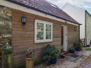 The exterior of a wooden house with a window and an open door with potted plants along a gravel path at The Wheelhouse in Beacon near Yarcombe