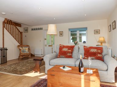 A living room with a gray sofa and red cushions a wooden chest used as a coffee table a wicker chair and staircase at The Wheelhouse Beacon near Yarcombe