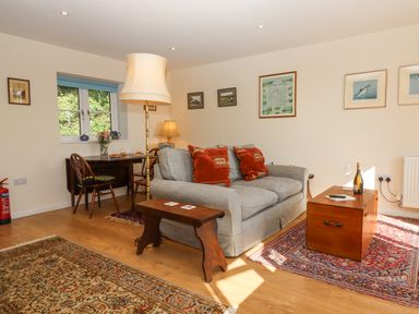 A living room with a gray sofa red cushions wooden coffee table and a dining table by the window at The Wheelhouse Beacon near Yarcombe