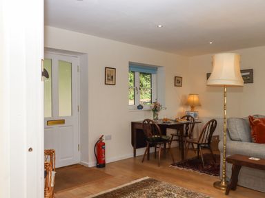 A room with a white door a small dining table with chairs a floor lamp and a sofa with cushions at The Wheelhouse Beacon near Yarcombe