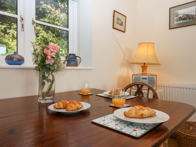 A dining table with plates of croissants glasses of orange juice and a vase of flowers near a window with decorative items on the sill at The Wheelhouse in Beacon near Yarcombe