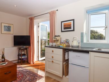 A kitchen area with coffee machine and kettle next to a window and door with curtains at The Wheelhouse Beacon near Yarcombe