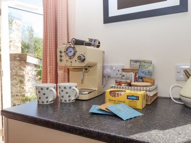 A kitchen counter with a cream coffee machine two mugs with bee patterns a box of biscuits and a basket with jars at The Wheelhouse Beacon near Yarcombe