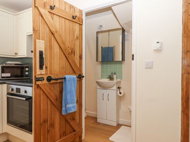 A kitchen with wooden door open to a bathroom with sink and mirror at The Wheelhouse Beacon near Yarcombe